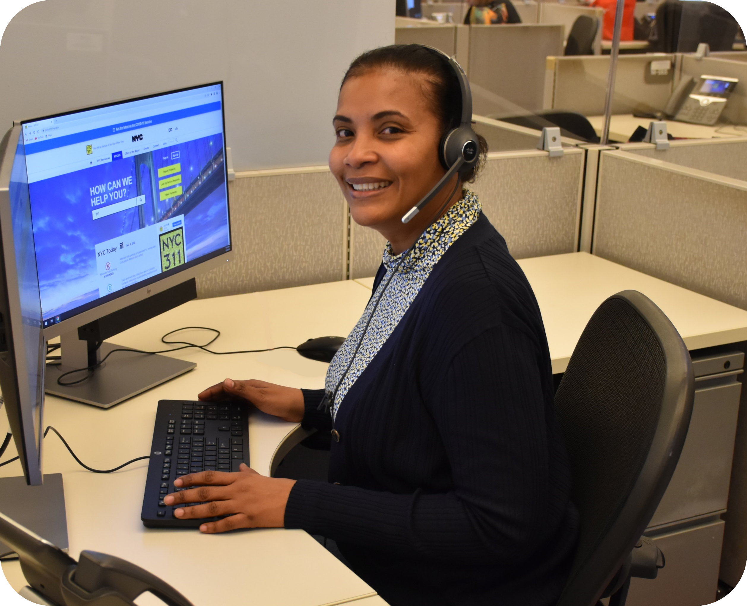 NYC311 Call Center Representative smiling and seated at a computer wearing a headset